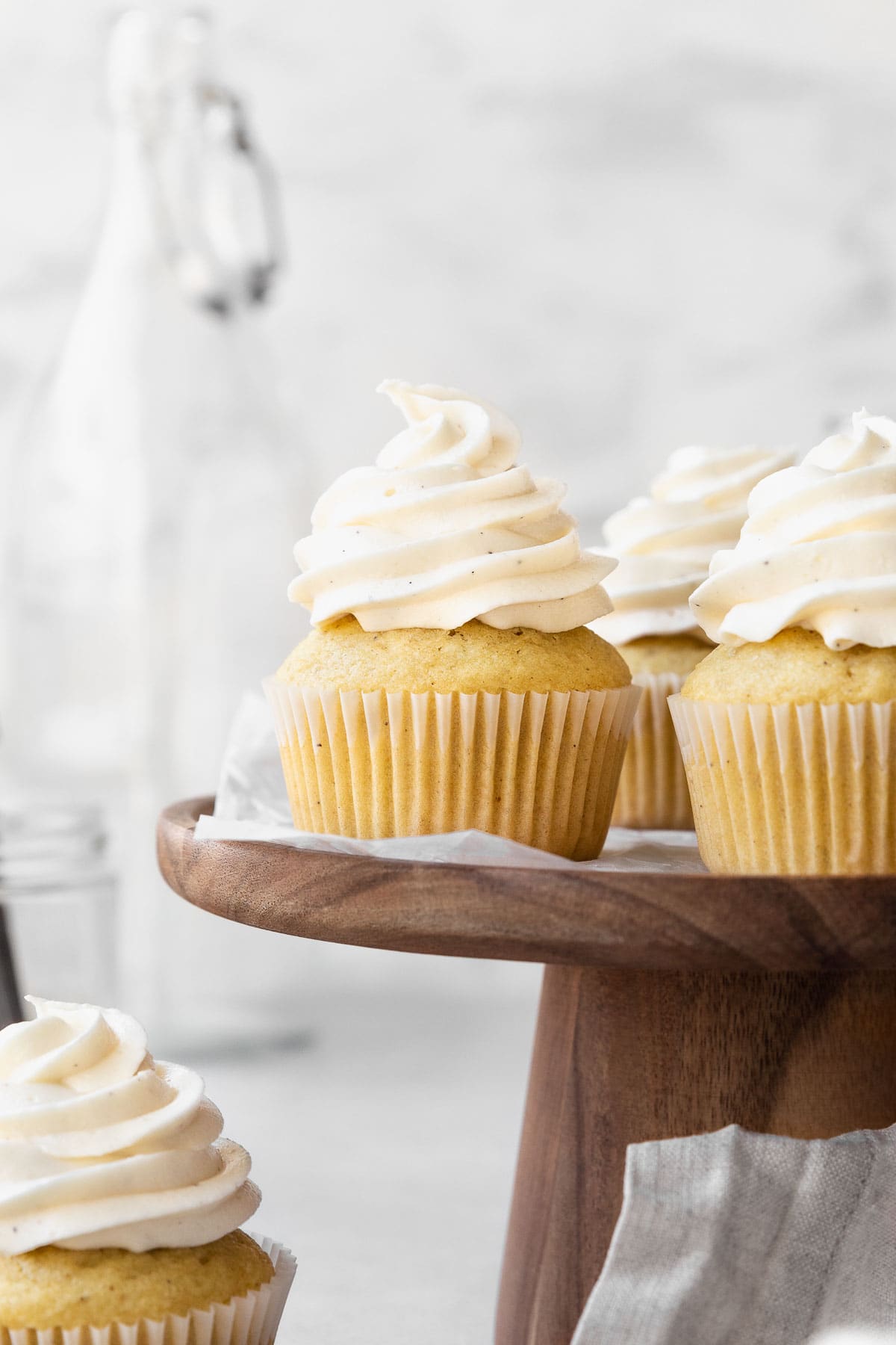 Side on shot of vanilla buttercream topped vegan cupcakes on a wooden cake platter.