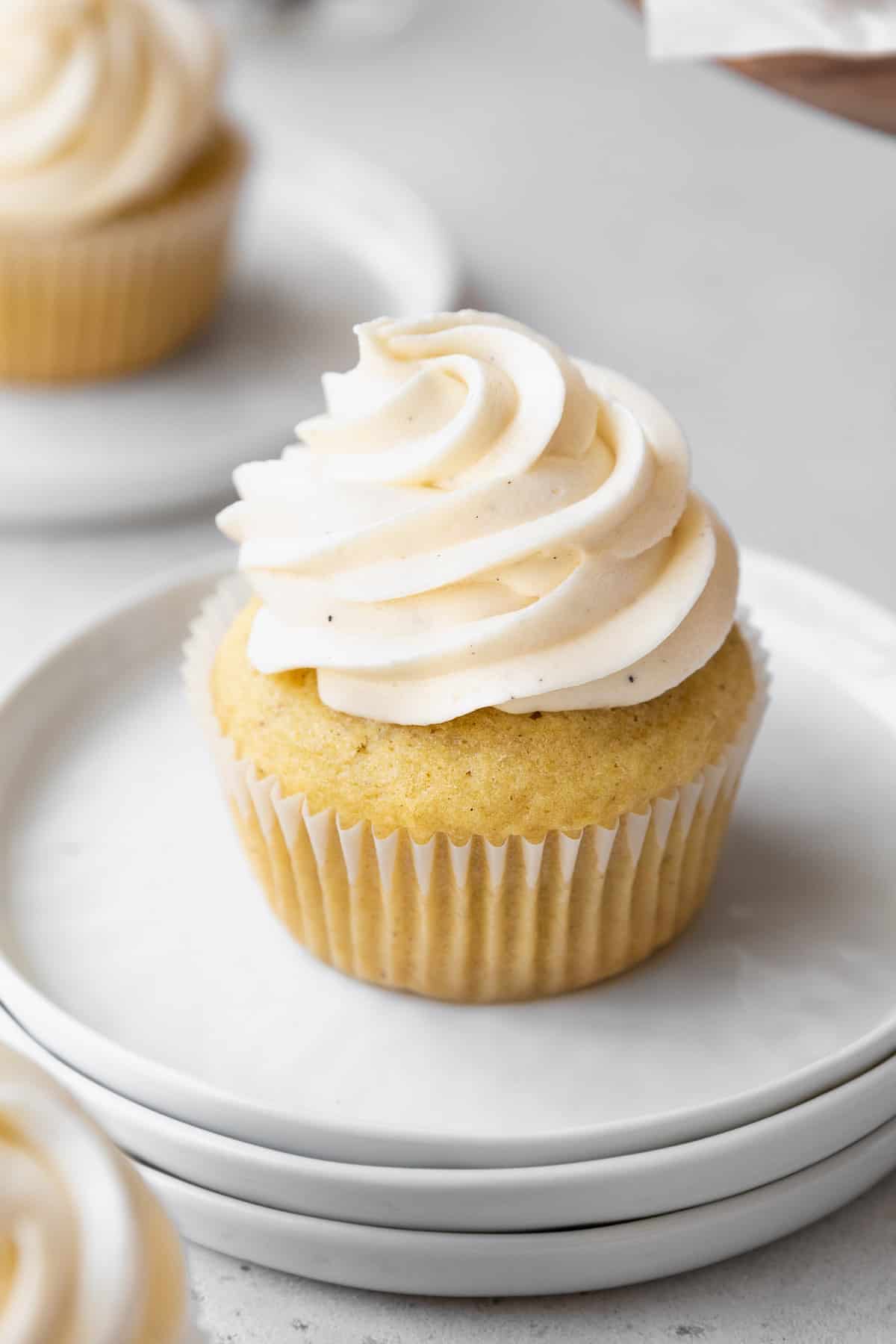 45 degree angle shot of dairy-free vegan frosting piped into a high swirl on homemade vanilla bean cupcakes.