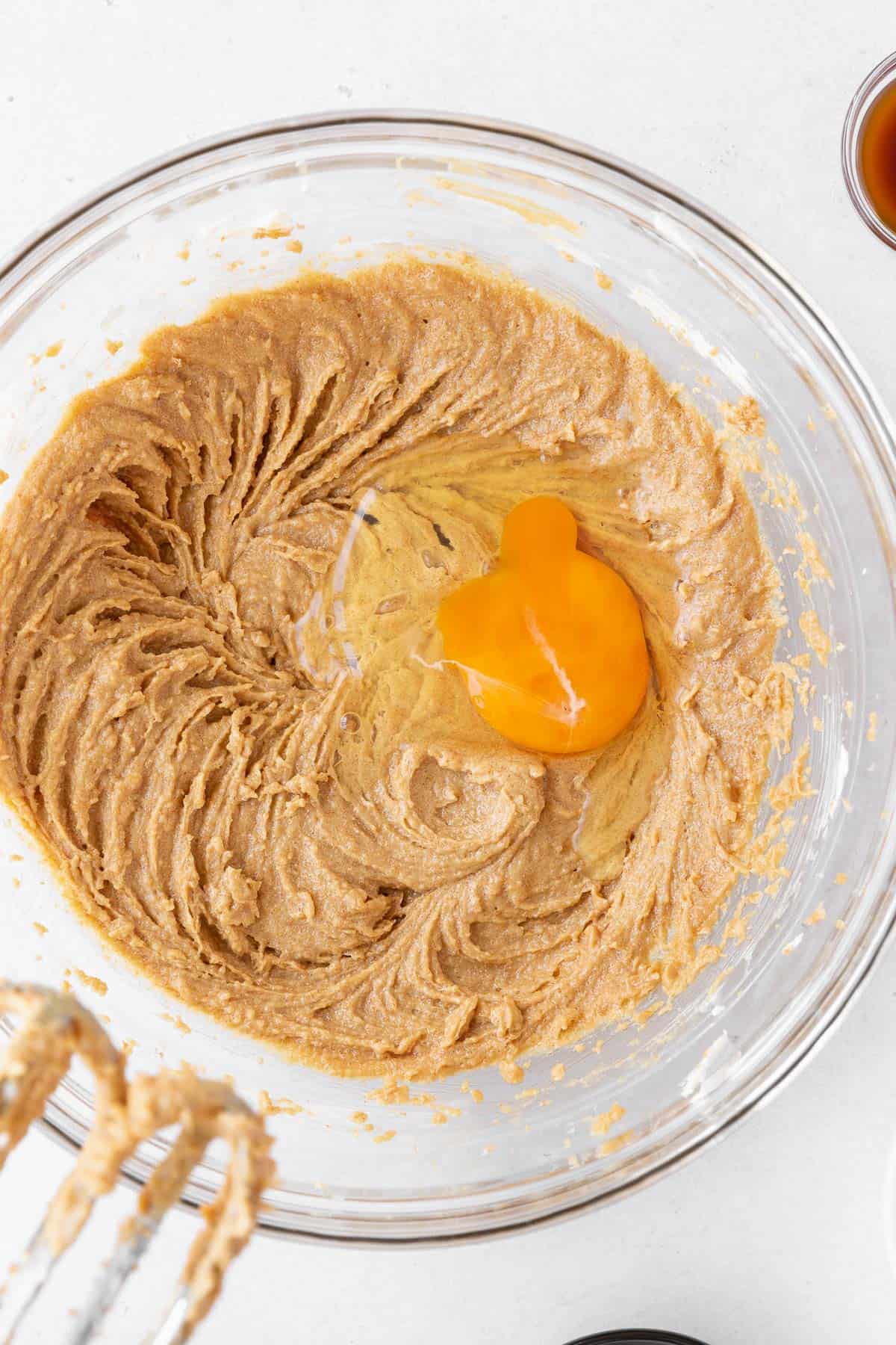 Adding an egg to the creamed peanut butter and butter in the mixing bowl. 