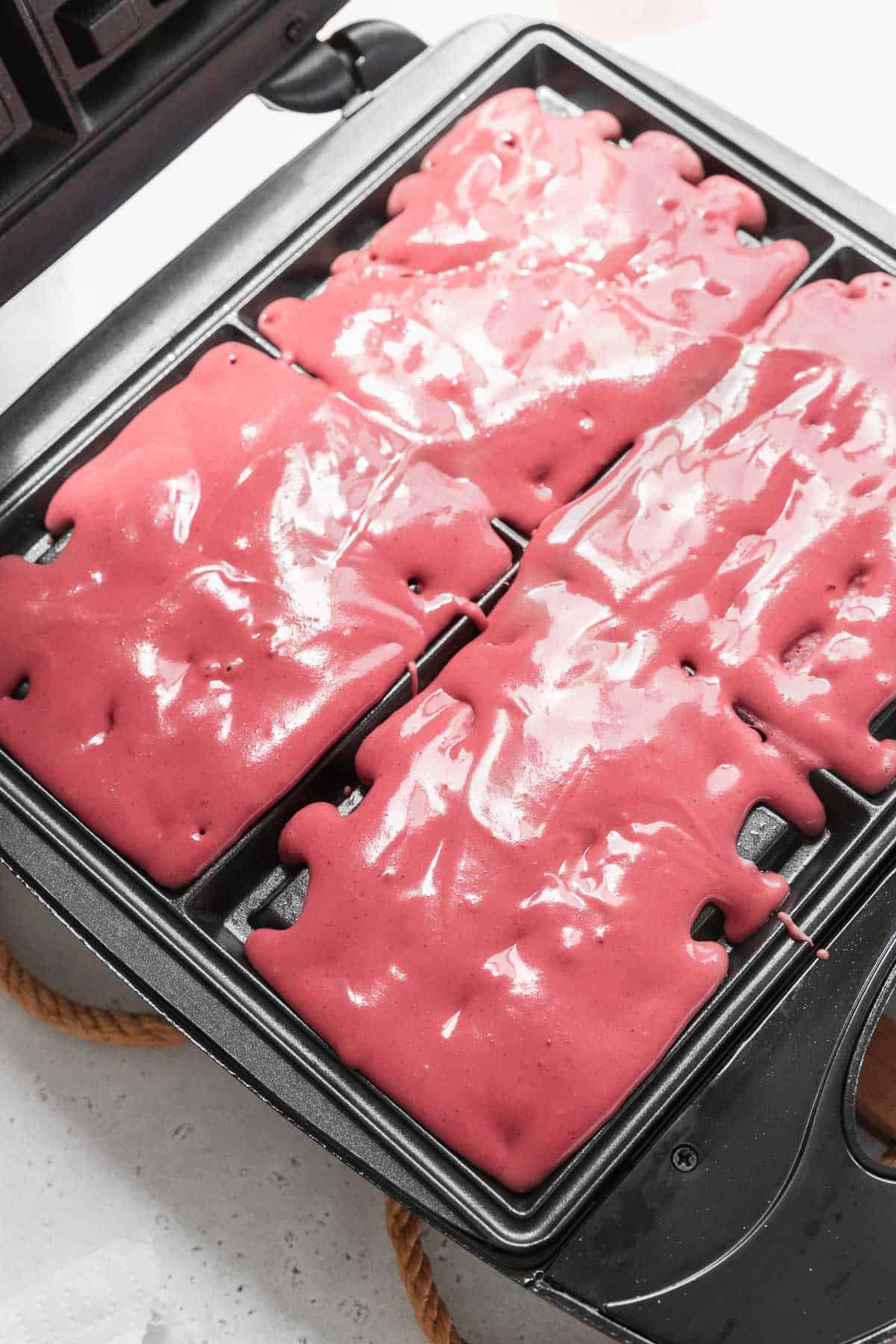 A waffle maker filled with red velvet waffle batter.