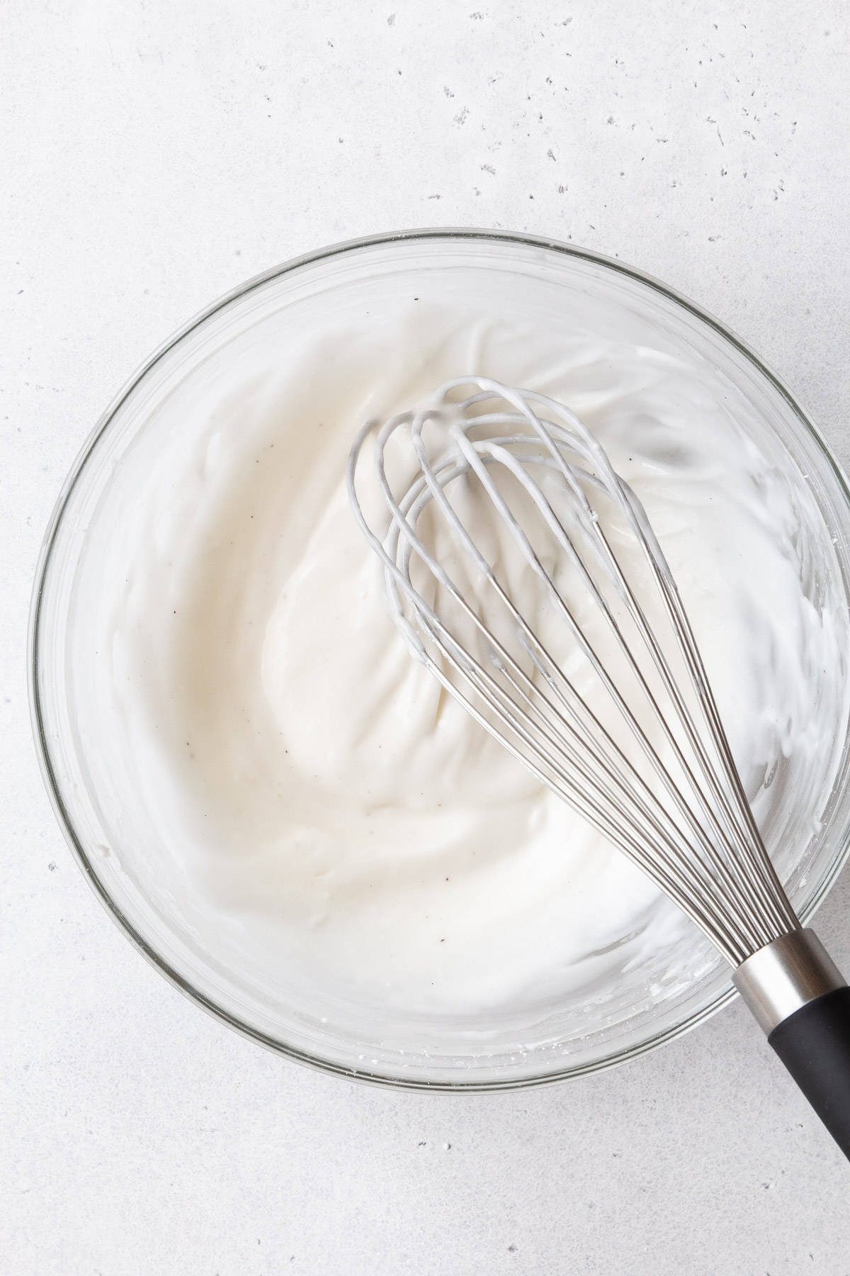 A glass mixing bowl of the cream cheese glaze with a whisk.