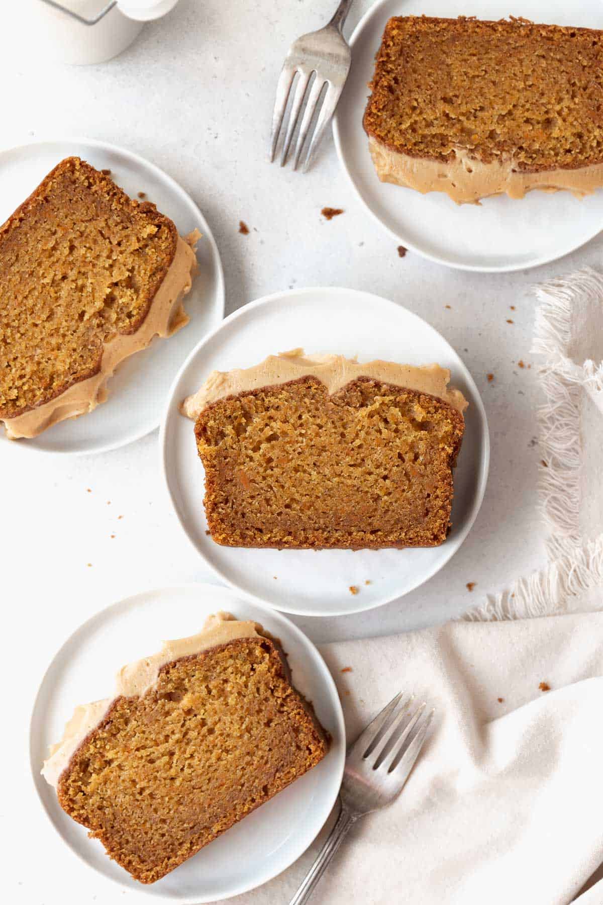 Overhead shot of sweet potato cake slices on white dessert plates with silver forks on a white surface.