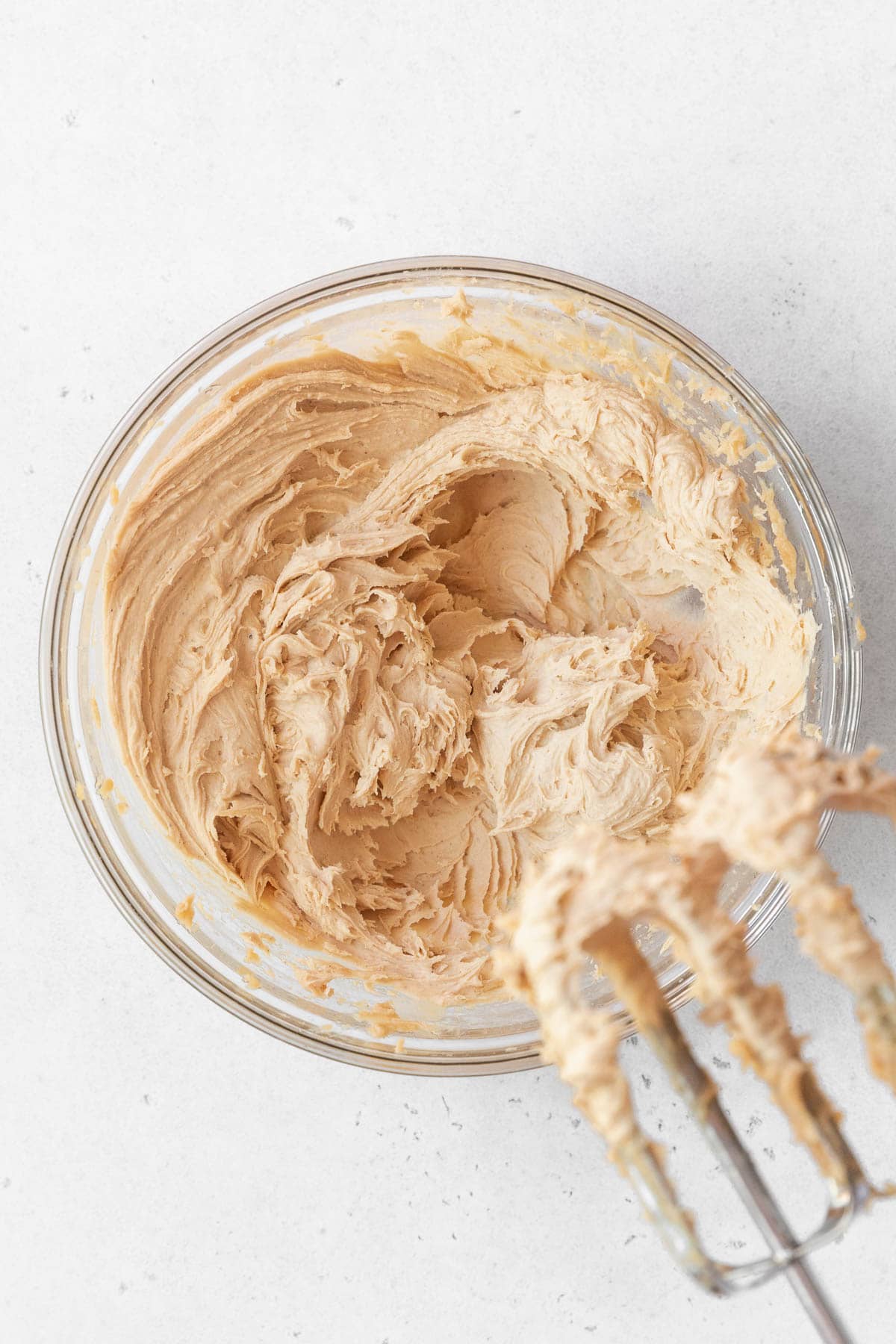 A glass bowl of cashew frosting whipped with a hand mixer.