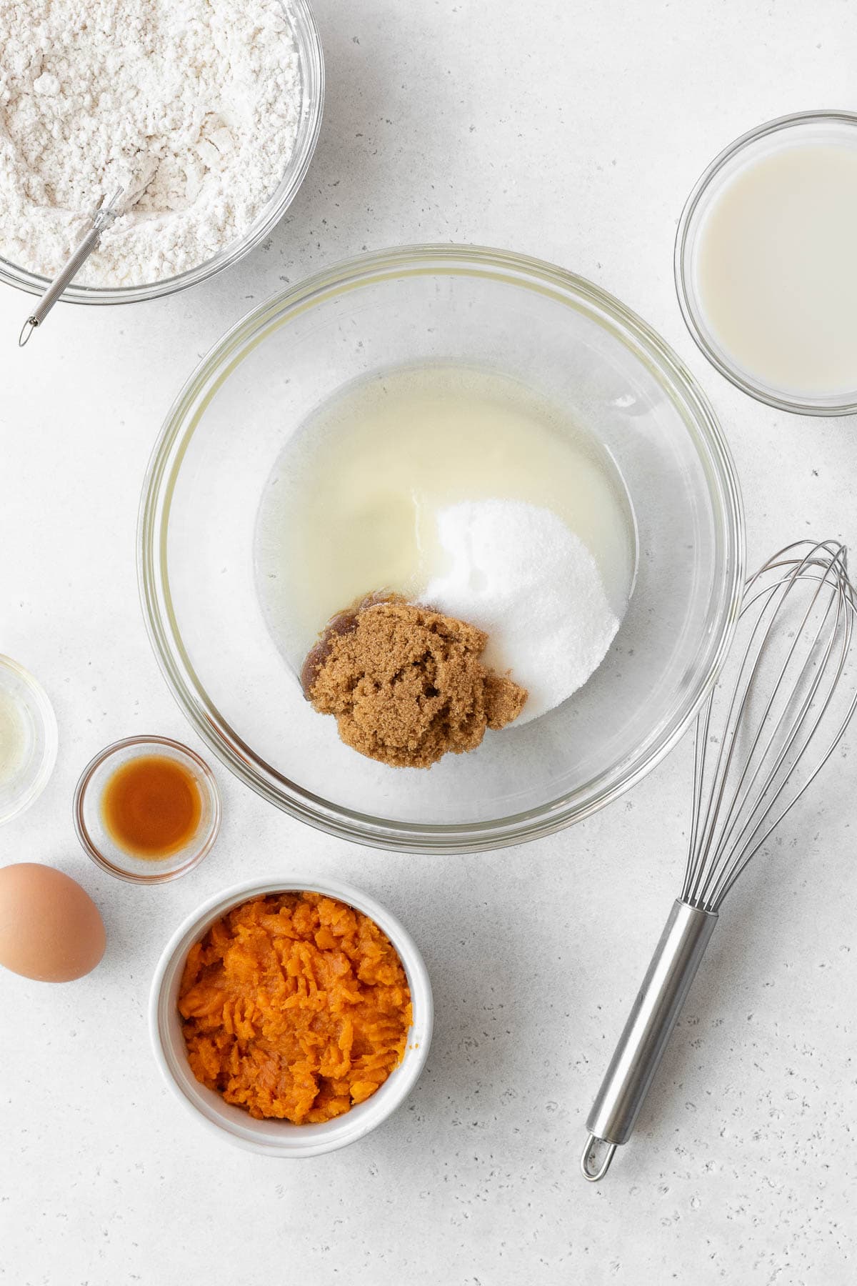 A large glass bowl with oil, granulated sugar, and brown sugar.