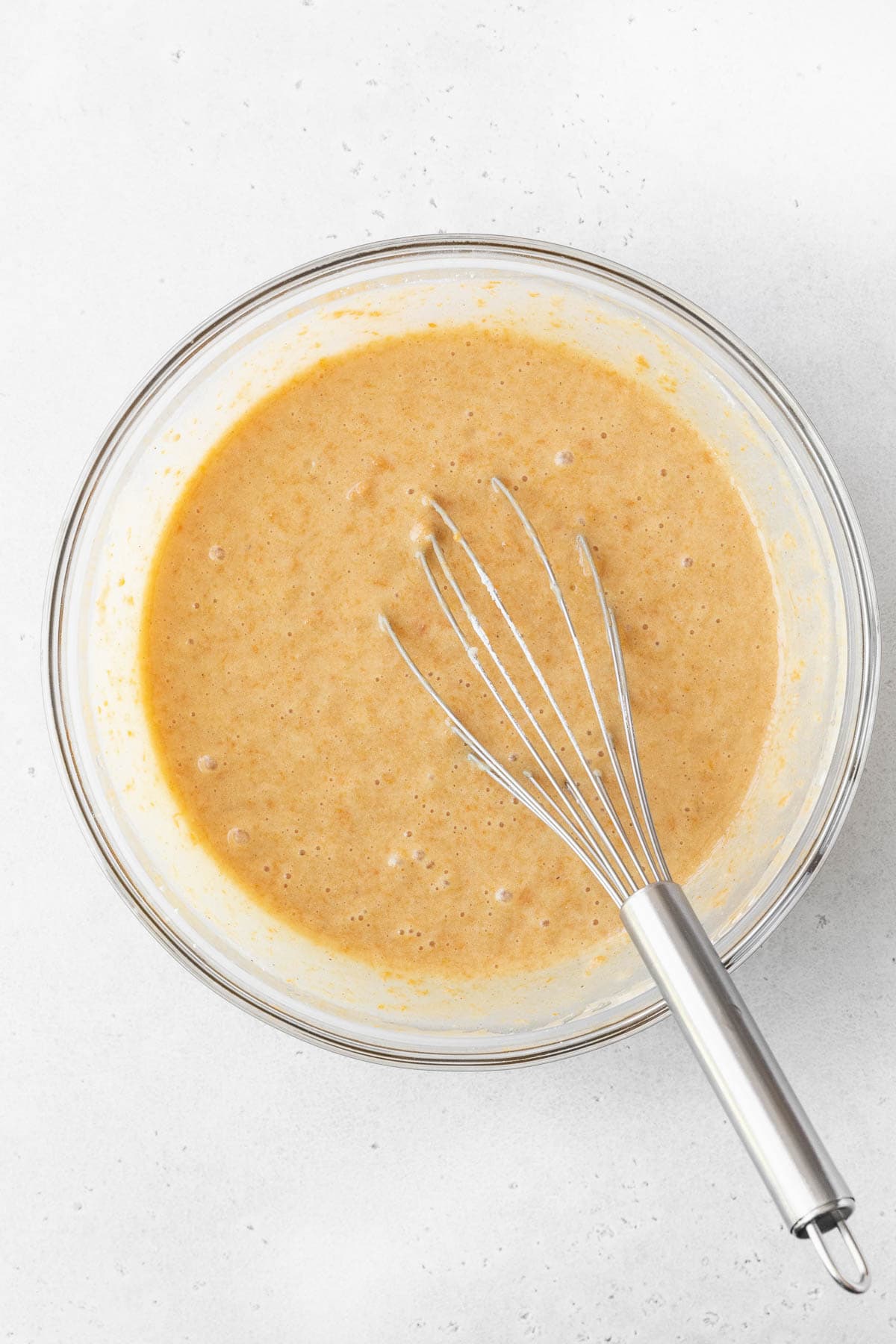 Healthy sweet potato cake batter in a glass bowl with a silver whisk.