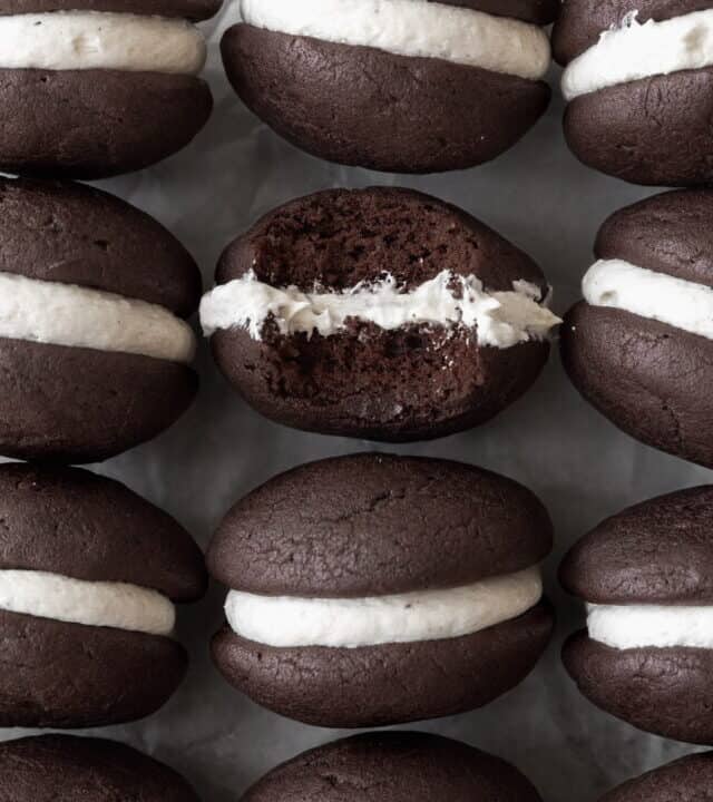 Gluten-free whoopie pies on a white sheet of parchment paper. One of the cookies has a bite taken out of it.