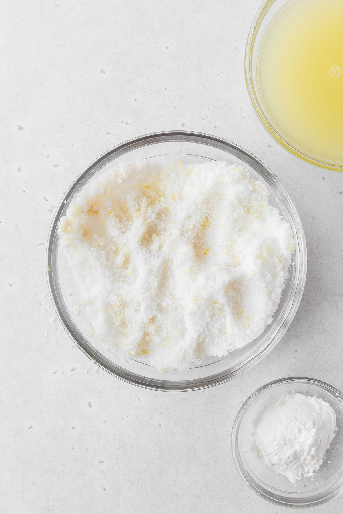A glass mixing bowl of sugar and lemon zest.