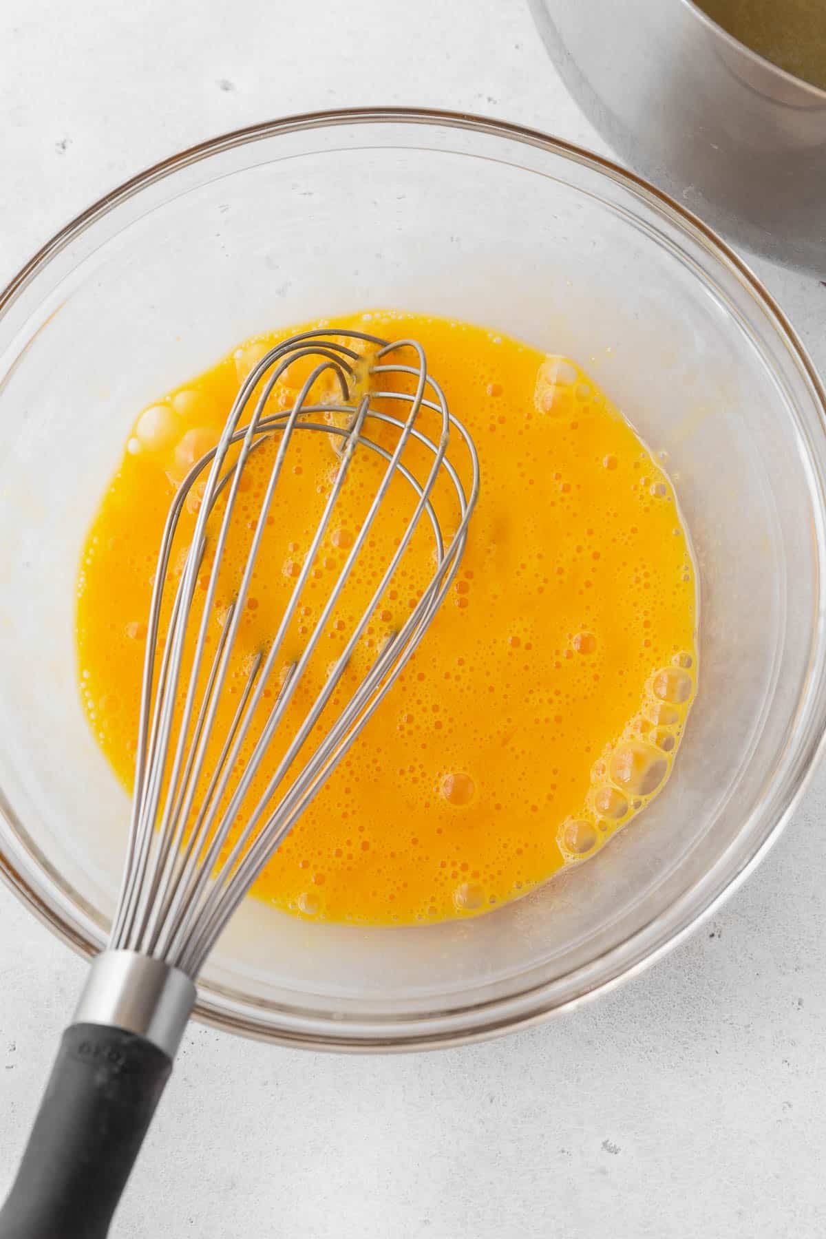 Whisked egg yolks in a glass bowl with a whisk.