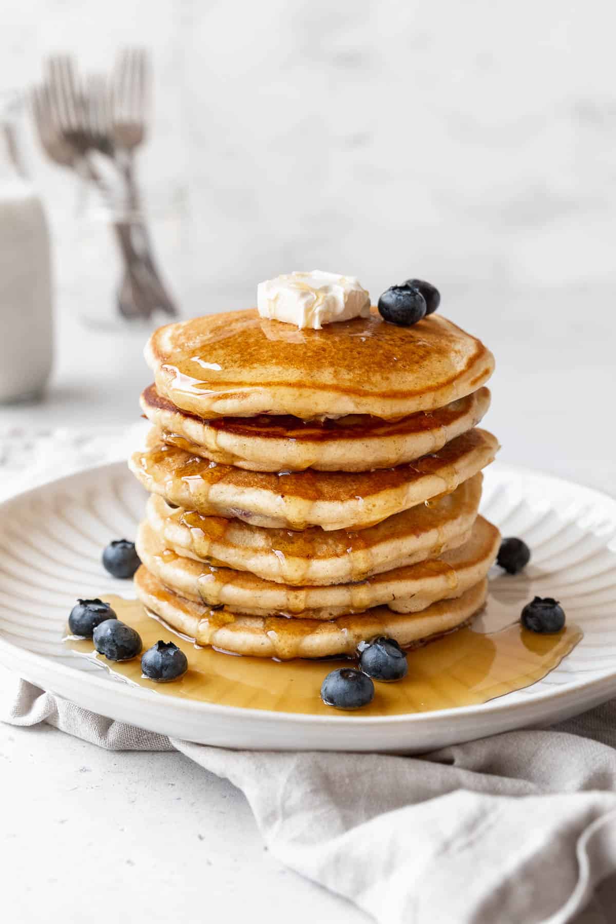 45 degree angle shot of a stack of muffin mix pancakes with blueberries, syrup, and butter.