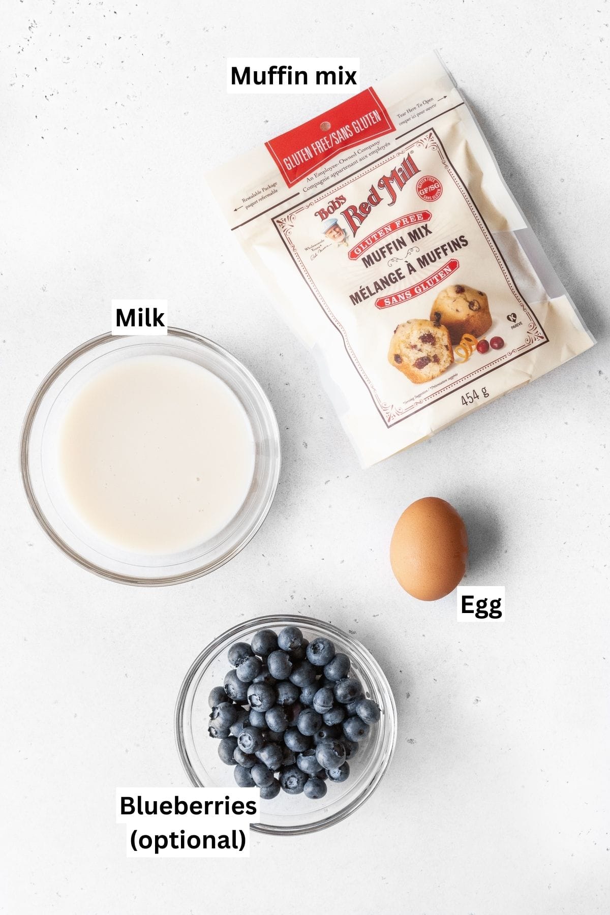 Ingredients needed to make muffin mix pancake measured out into bowls on a white table.