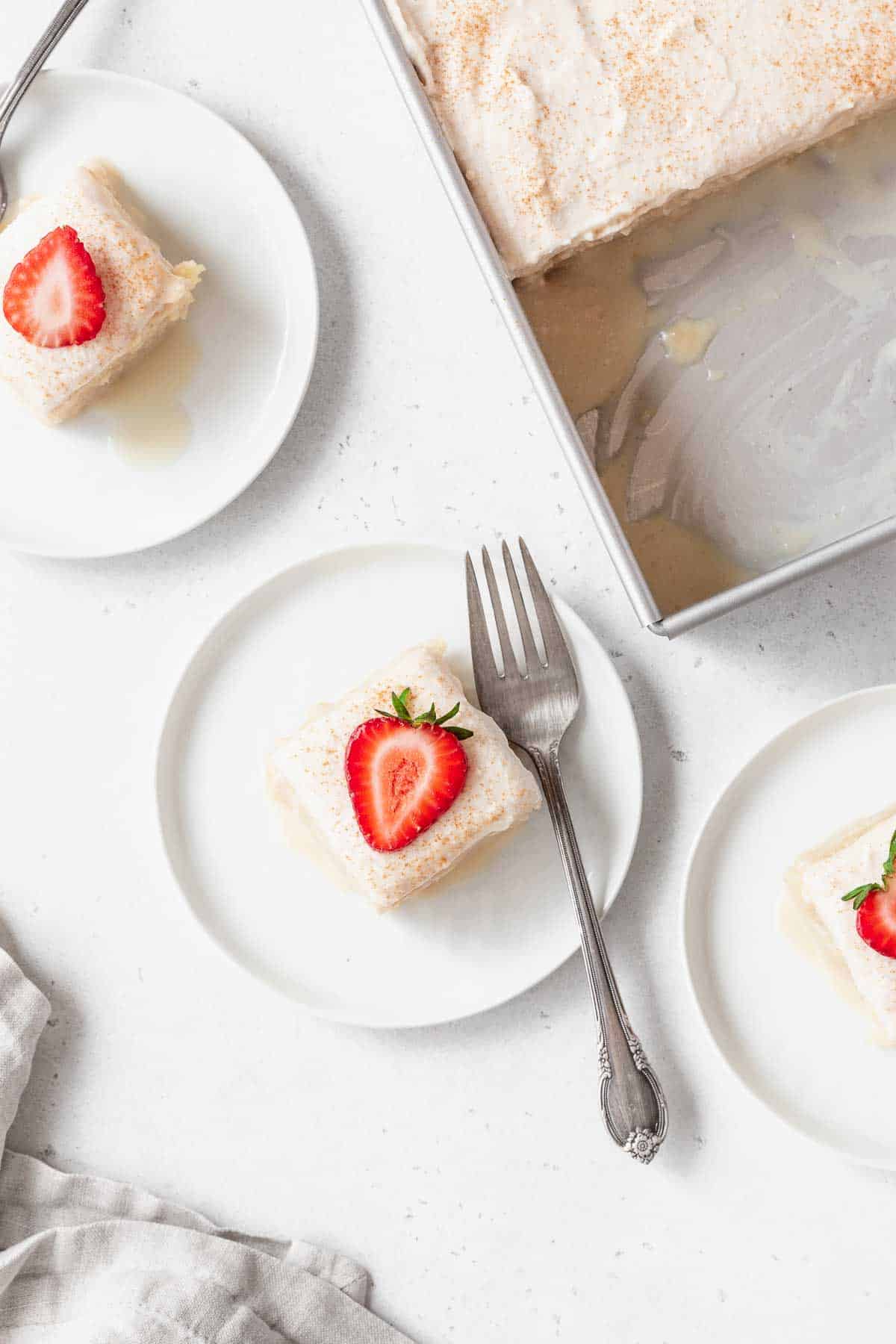An overhead shot of a few small dessert plates of gluten-free tres leches cake next to a pan of the cake.