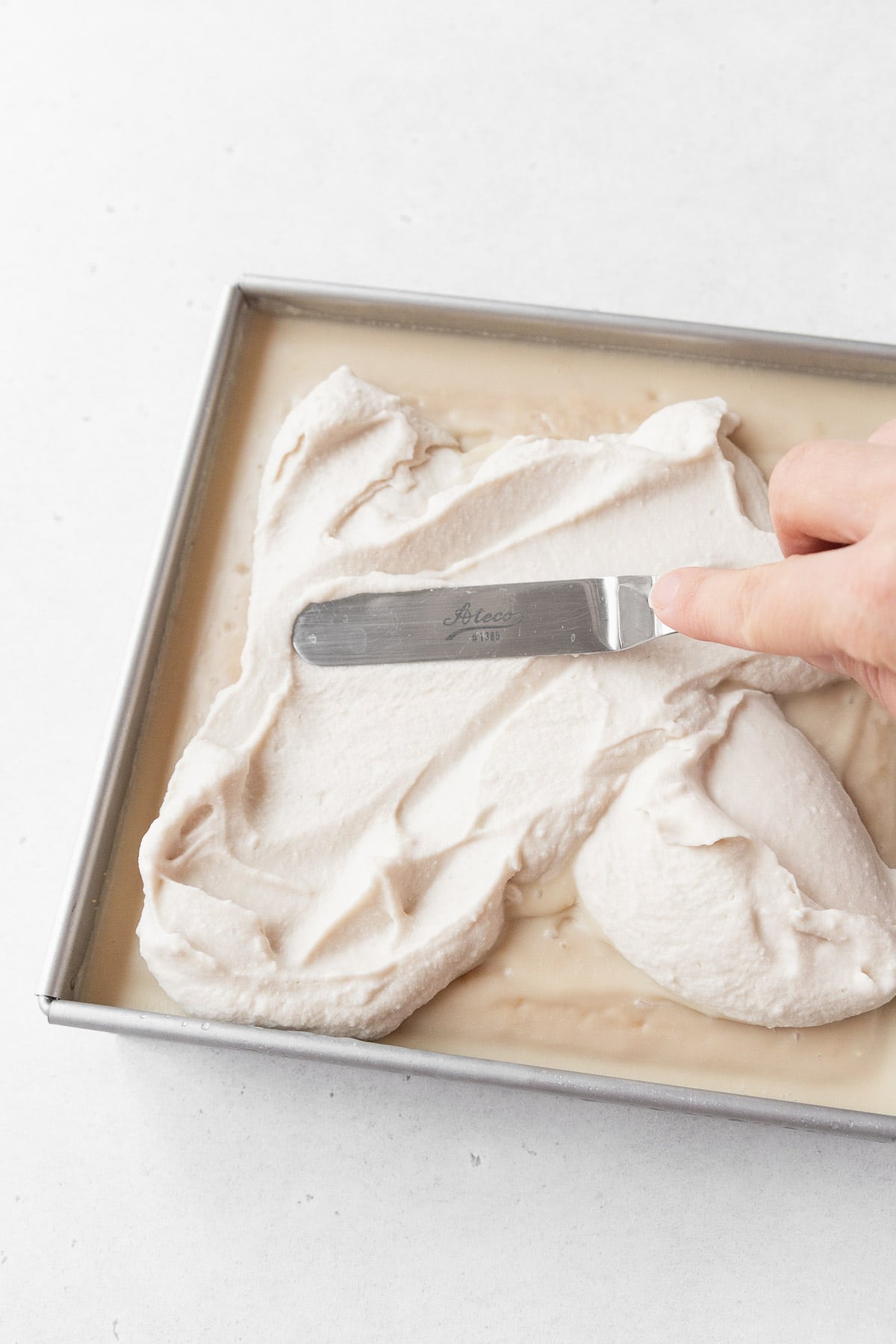 Spreading the non-dairy whipped cream on the gluten-free and dairy-free tres leches cake.