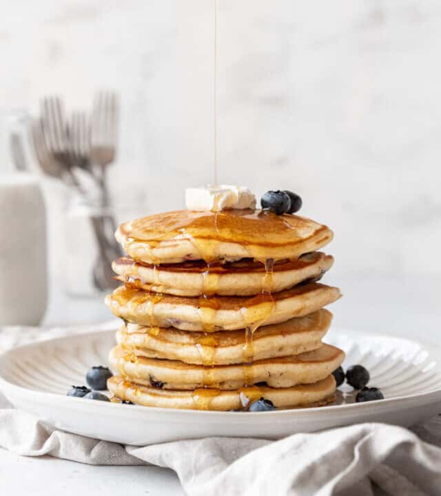 distance side-on action shot of syrup being drizzled on a shortstack of blueberry studded muffin mix pancakes.