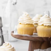 Square hero shot of a dairy free vanilla cupcakes on a wooden cake stand.