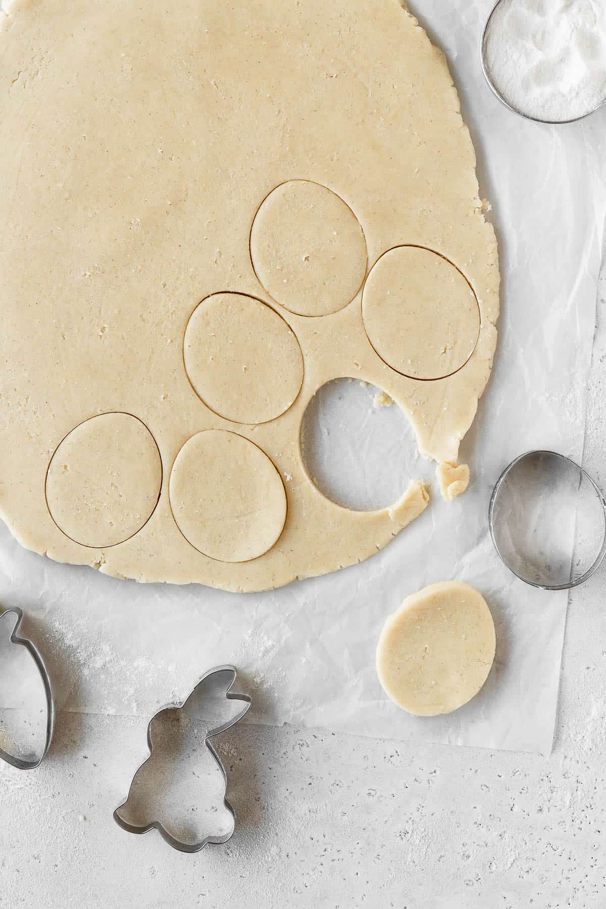 Sugar cookie dough rolled out and shapes being cut with a cookie cutter.