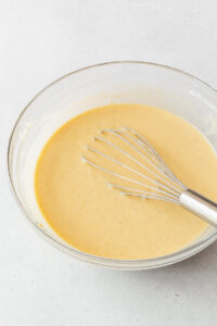 A whisked bowl of the gluten-free pineapple cake batter with a whisk in it.