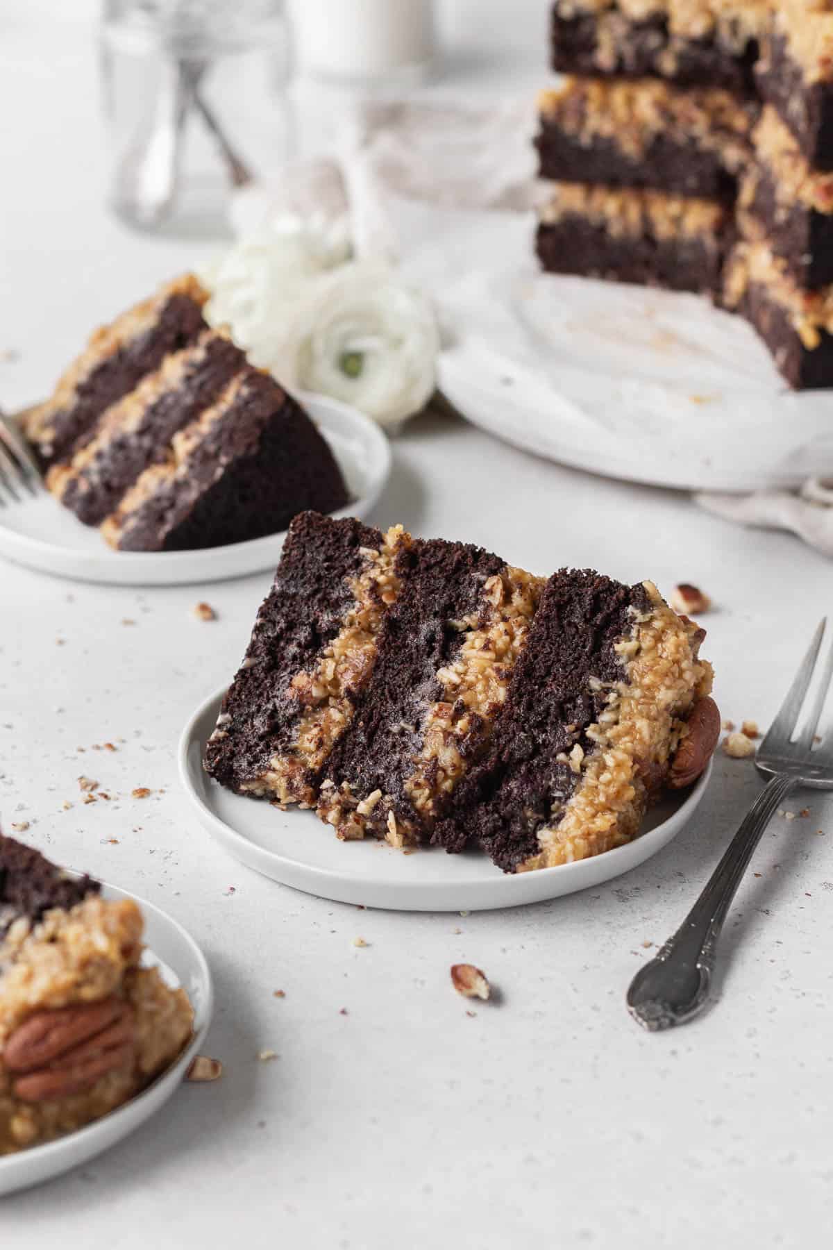 A slice of gluten-free German chocolate cake on a white dessert plate with a fork next to it.