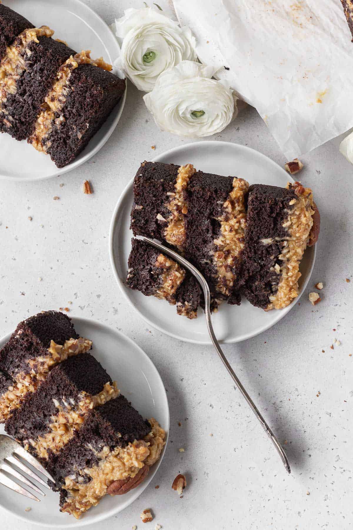 An overhead shot of three small white plates with a slice of gluten free German chocolate cake placed on each one.