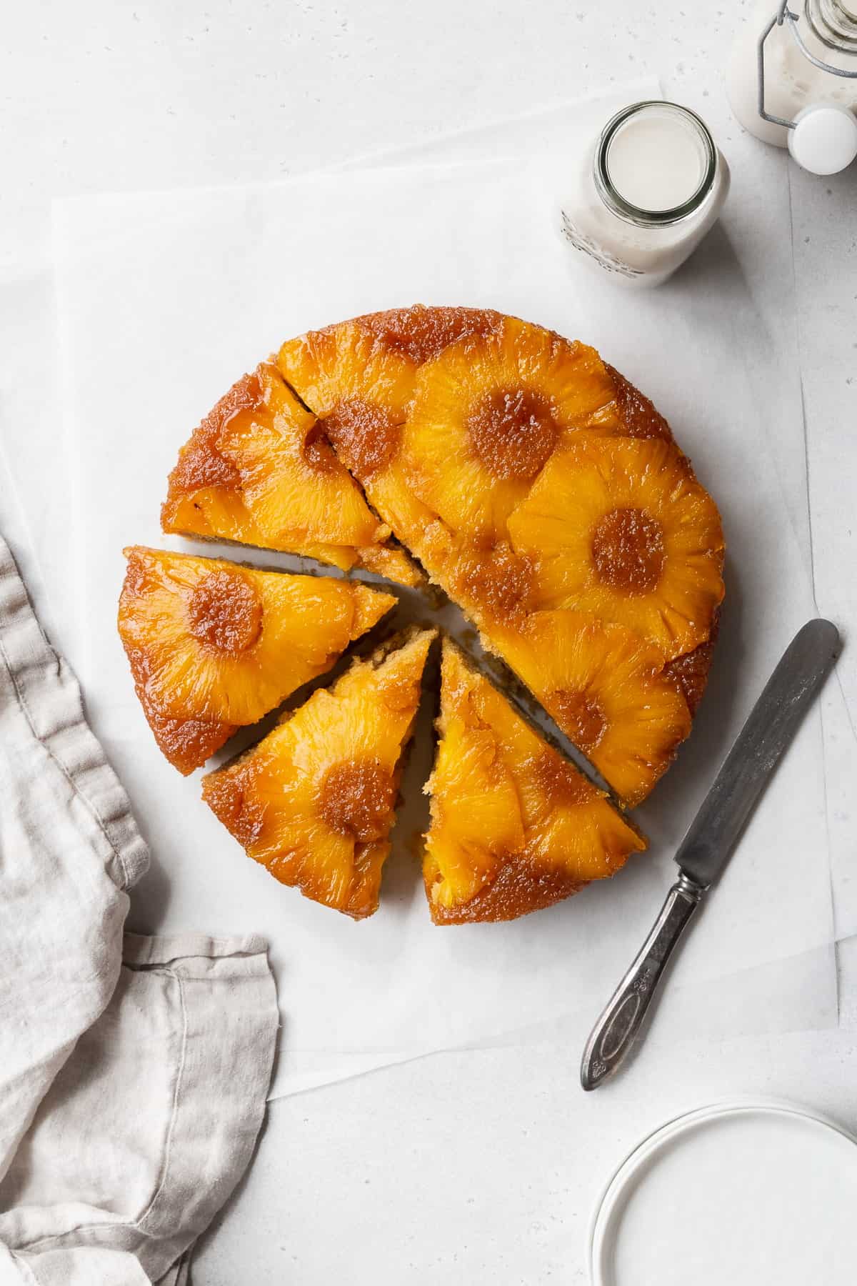 A sliced gluten-free pineapple cake on the counter with a napkin and bottle of milk.