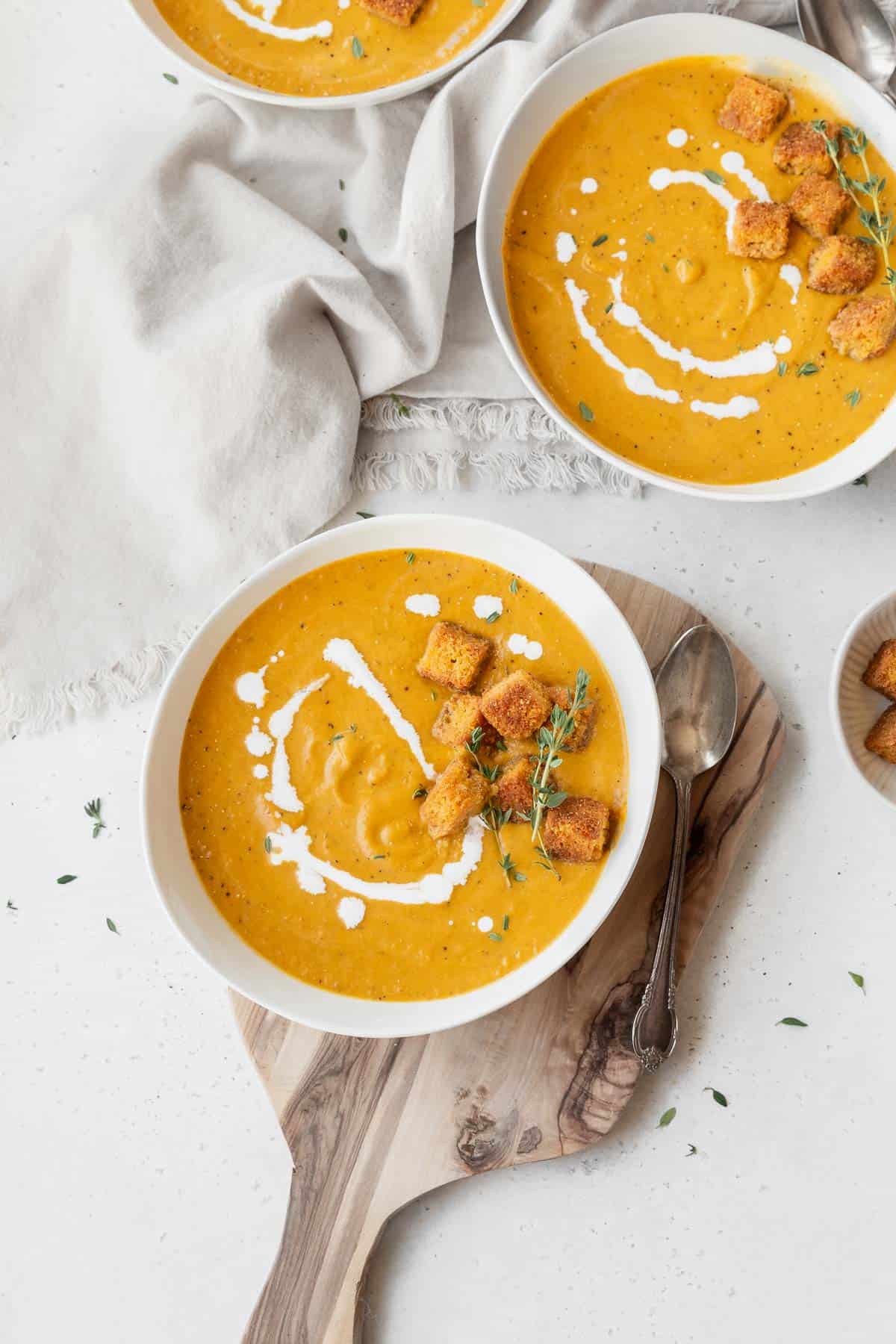 Overhead shot of 3 bowls of creamy vegan pumpkin soup garnished with cornbread croutons and fresh thyme.
