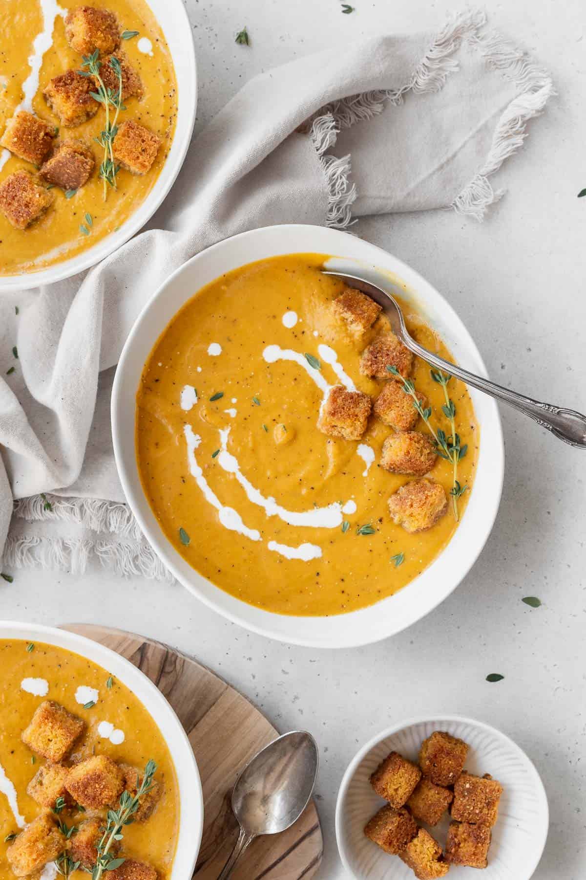 Overhead shot of a bowl of vegan pumpkin bisque soup garnished with fresh thyme, cornbread croutons, and a drizzle of vegan cream.