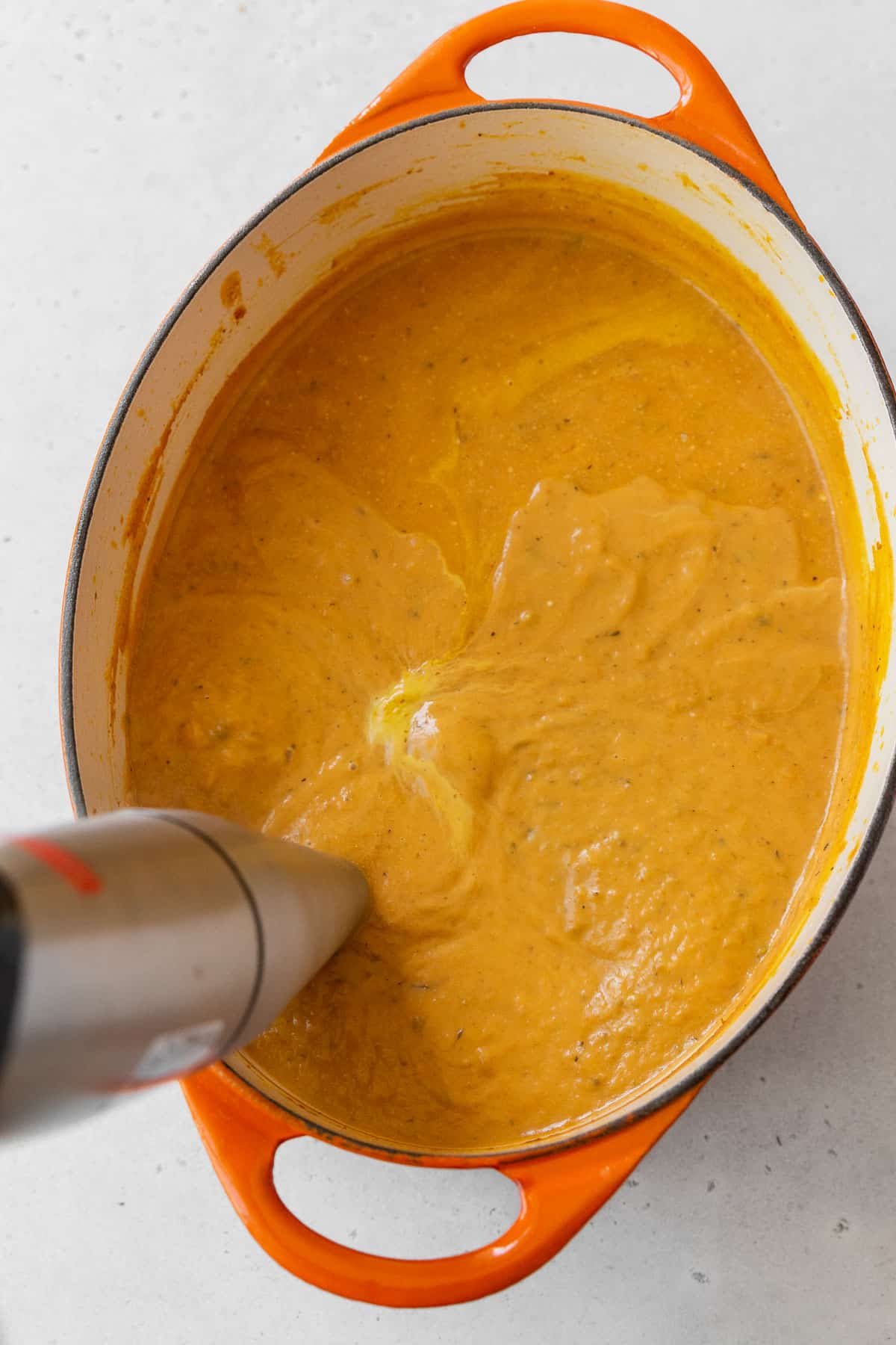 Using an immersion blender to purée the gluten-free and vegan pumpkin bisque soup.