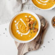 Overhead shot of a bowl of vegan pumpkin bisque garnished with thyme, croutons, and a drizzle of vegan cream.