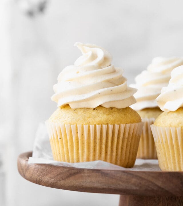 Dairy-free vanilla cupcakes on a wooden cake stand.