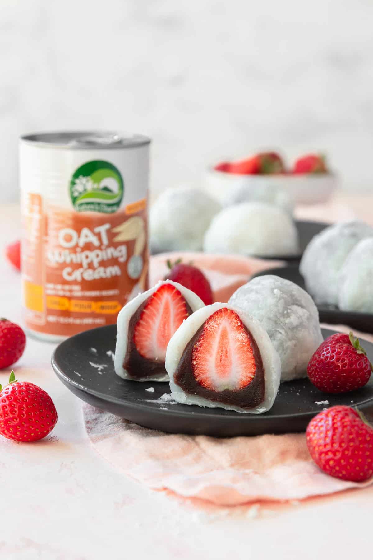 Sliced strawberry mochi on a plate with a can of oat whipping cream in the background.