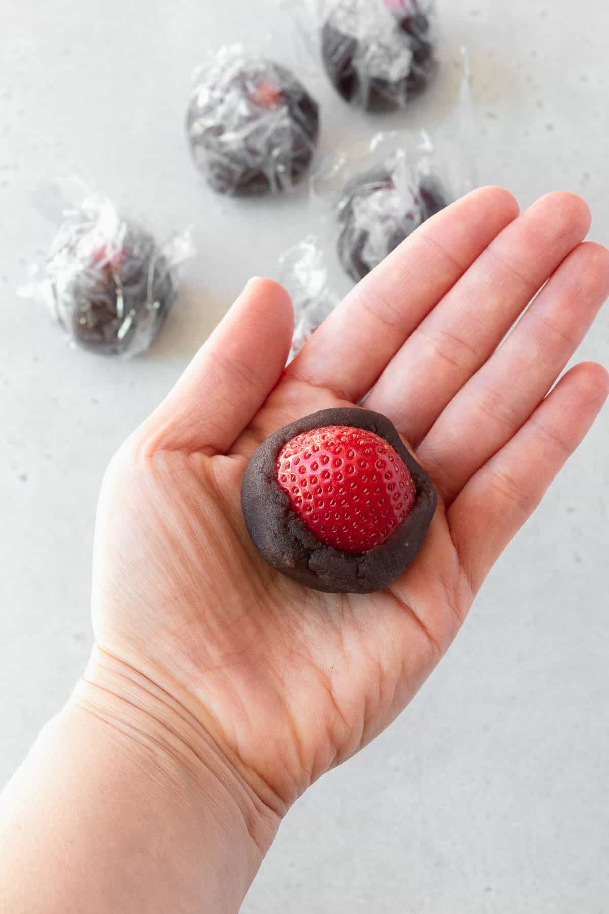 A hand holding a strawberry halfway wrapped in sweetened red bean paste.