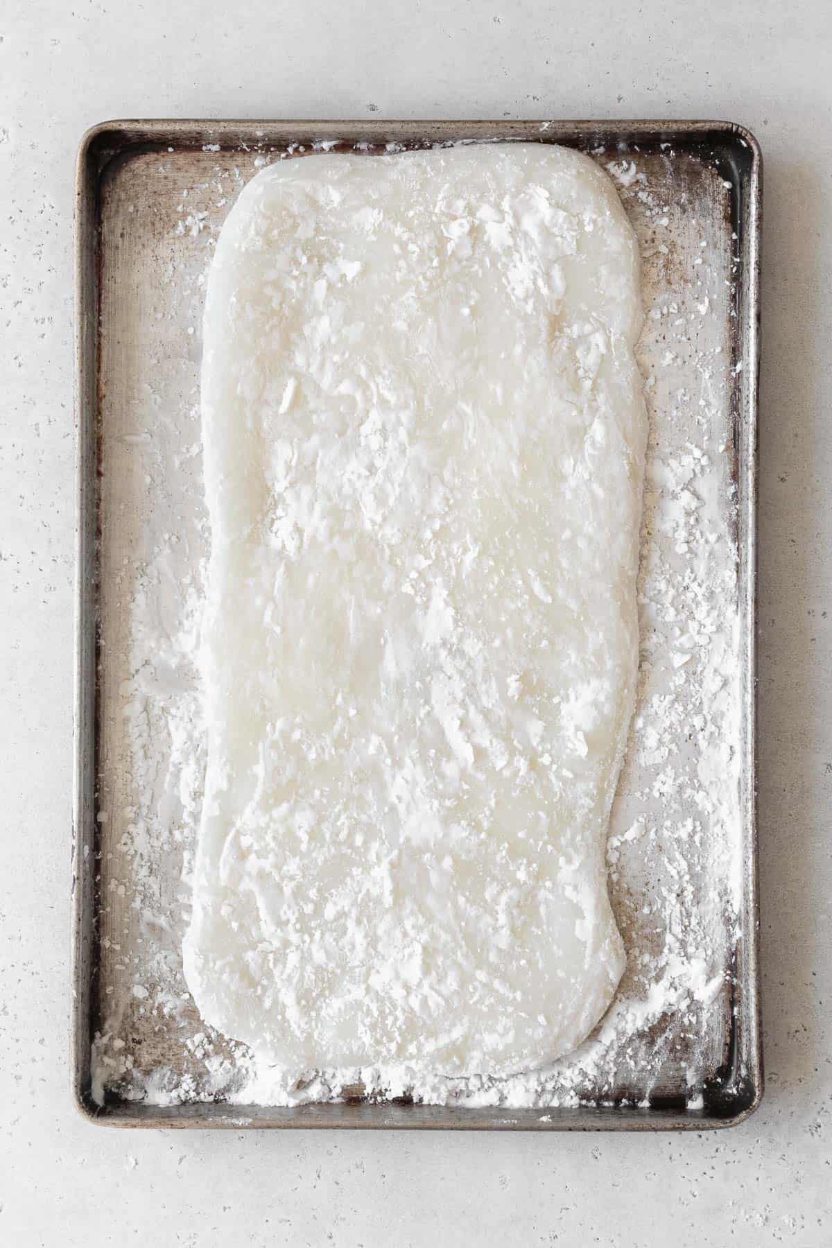 Mochi flatted out into a rectangle on a baking sheet dusted with potato starch.