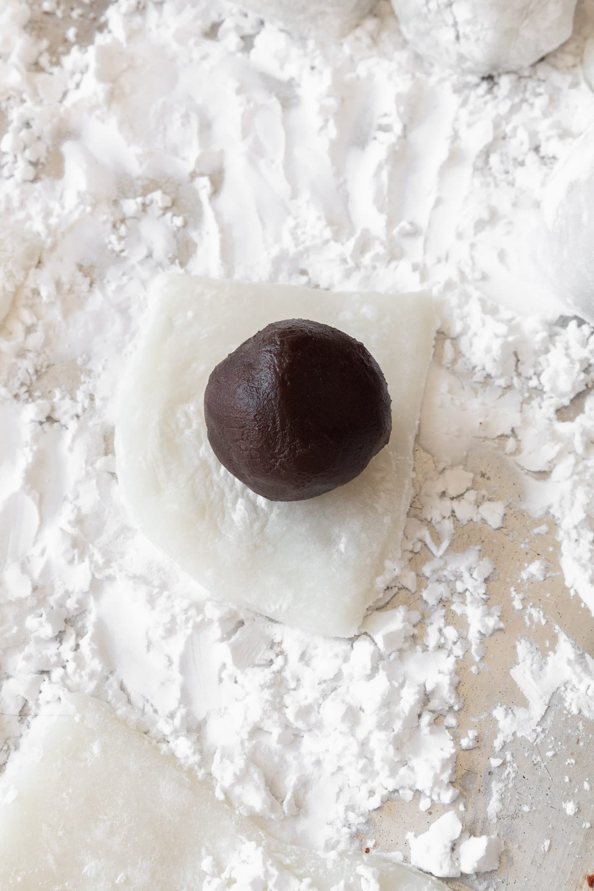 A ball of sweet red bean paste placed on a square of mochi to be wrapped in.