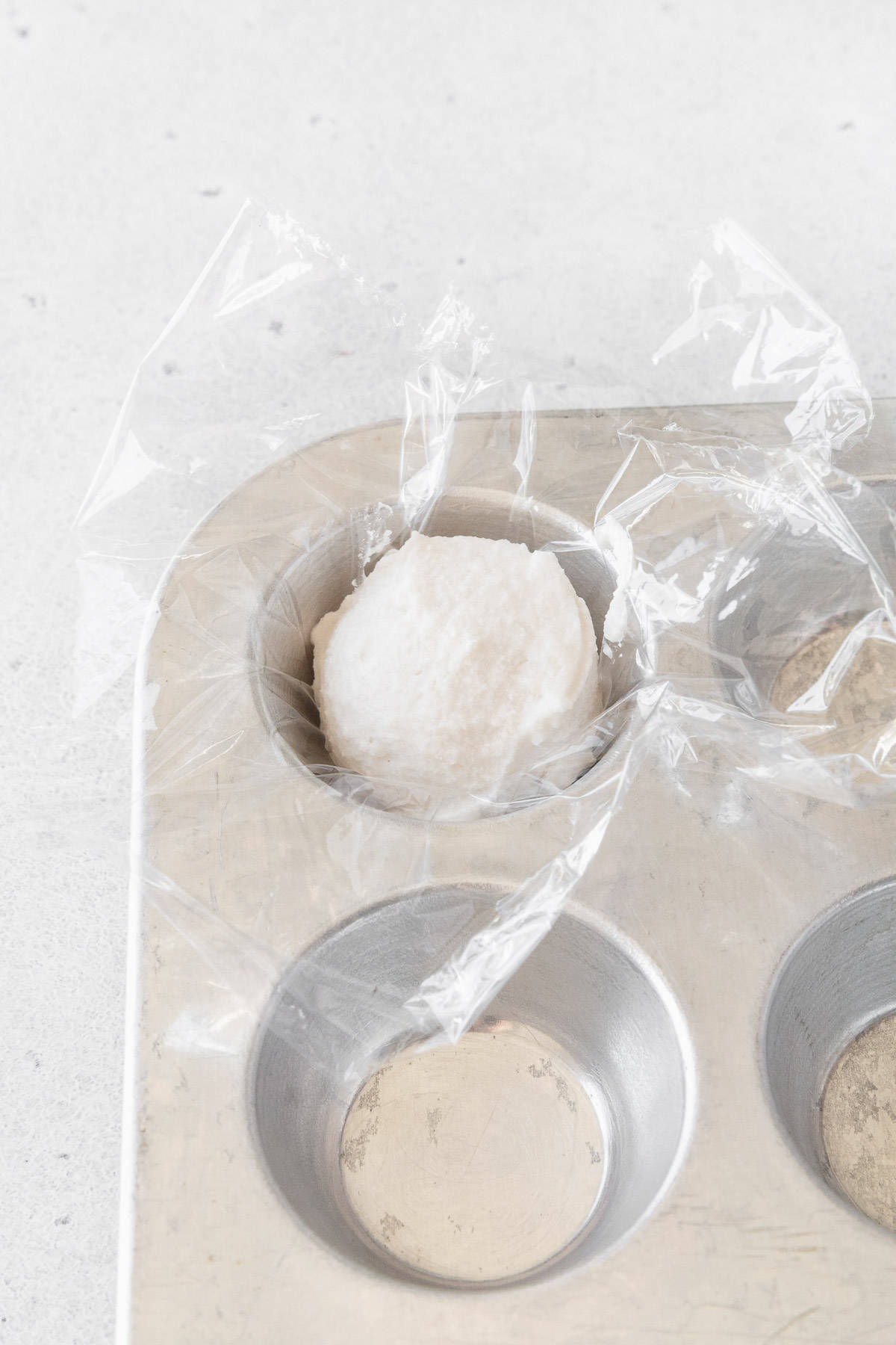 A portion of oat whipping cream in a mini muffin tin lined with plastic wrap.