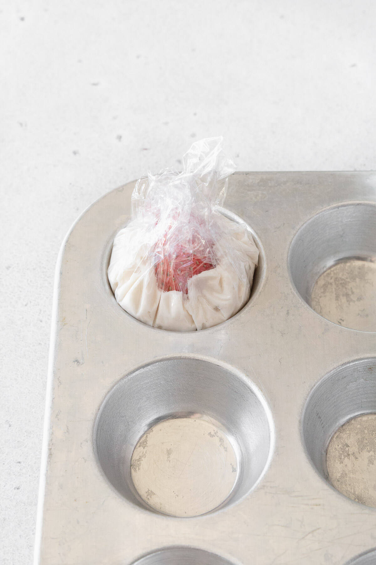 Plastic wrap twisted over a strawberry and some whipped cream in a mini muffin tin.