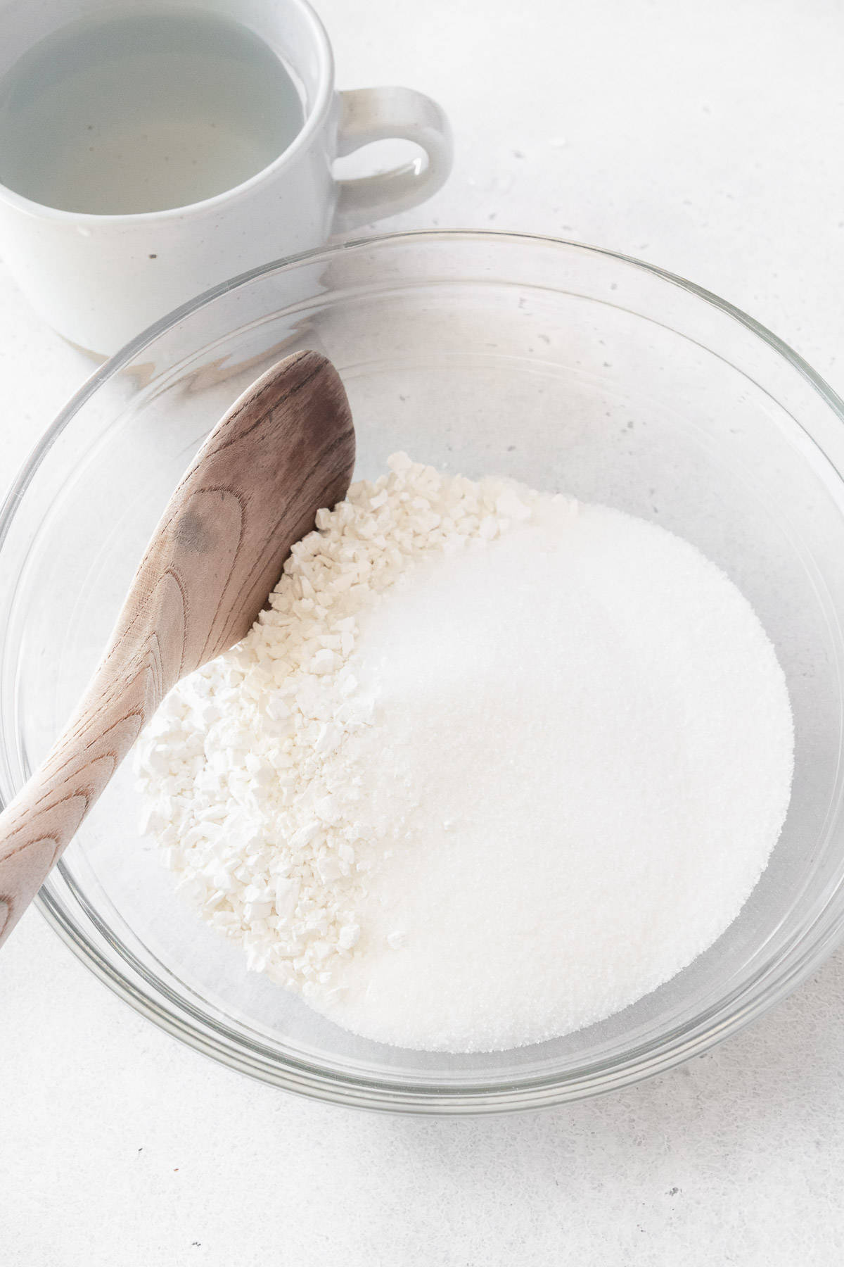 Shiratamako and sugar in a glass bowl with a mug of water next to it.