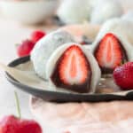 A sliced strawberry mochi on a black plate.