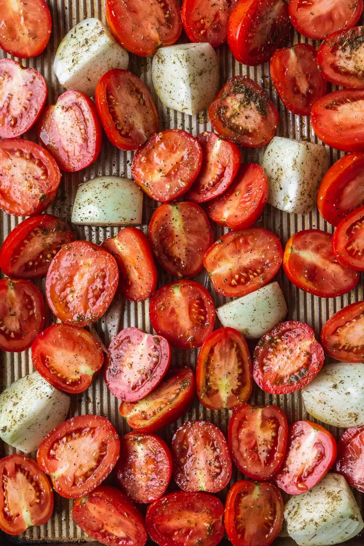 Fresh tomatoes sliced in half and chopped onions on a baking sheet.