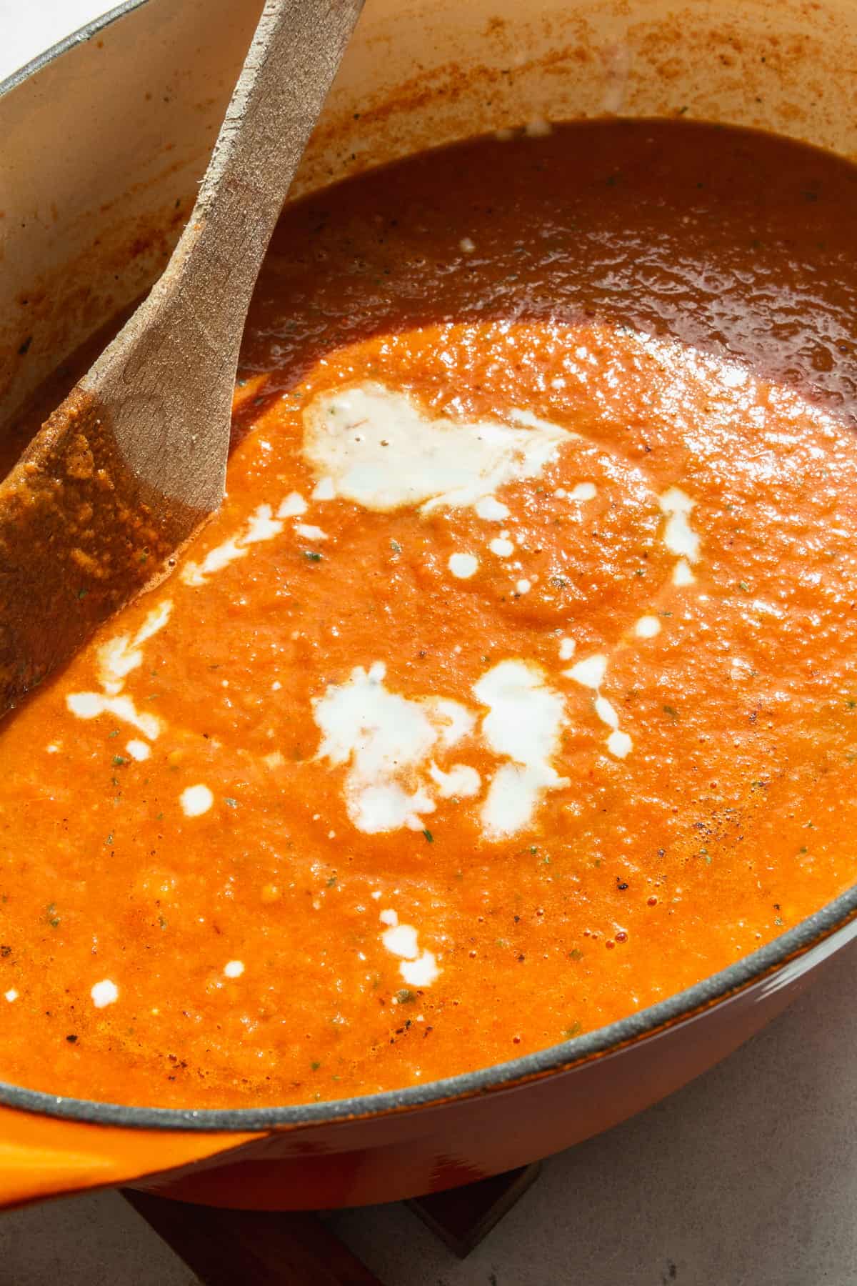 A pot of blended tomato basil soup with a swirl of coconut milk.