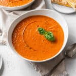 A bowl of vegan tomato soup with a drizzle of olive oil and a sprig of basil.