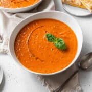 A bowl of vegan tomato soup with a drizzle of olive oil and a sprig of basil.