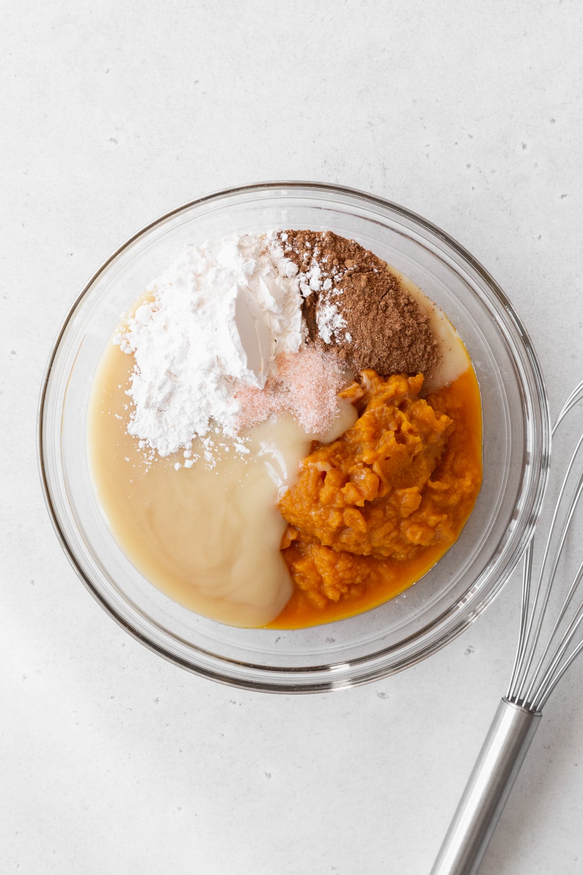 Pumpkin pie filling ingredients in a glass bowl next to a wire whisk.