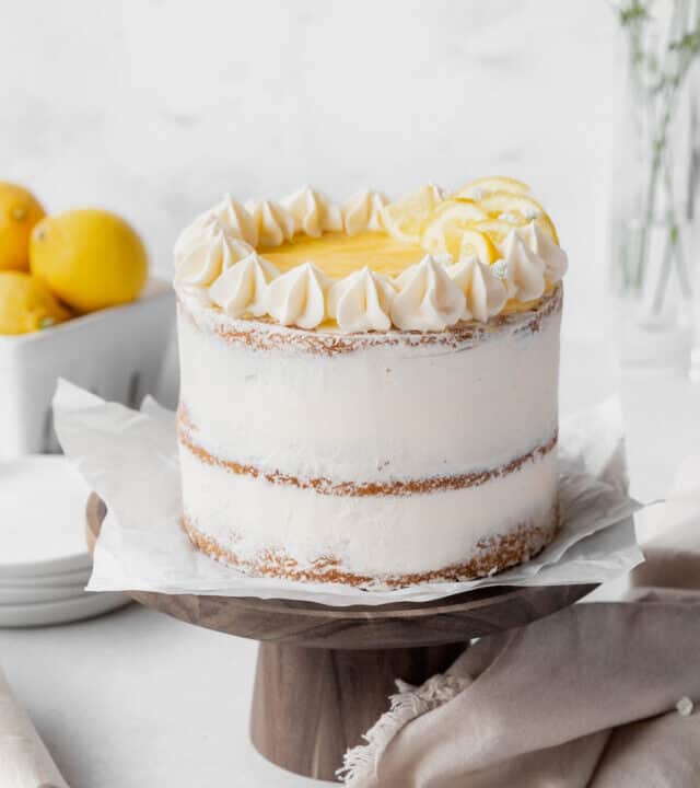 final flourishes added to the dairy-free lemon curd cake including rosettes of lemon buttercream, a center topping of lemon curd, and candied lemons as decoration.