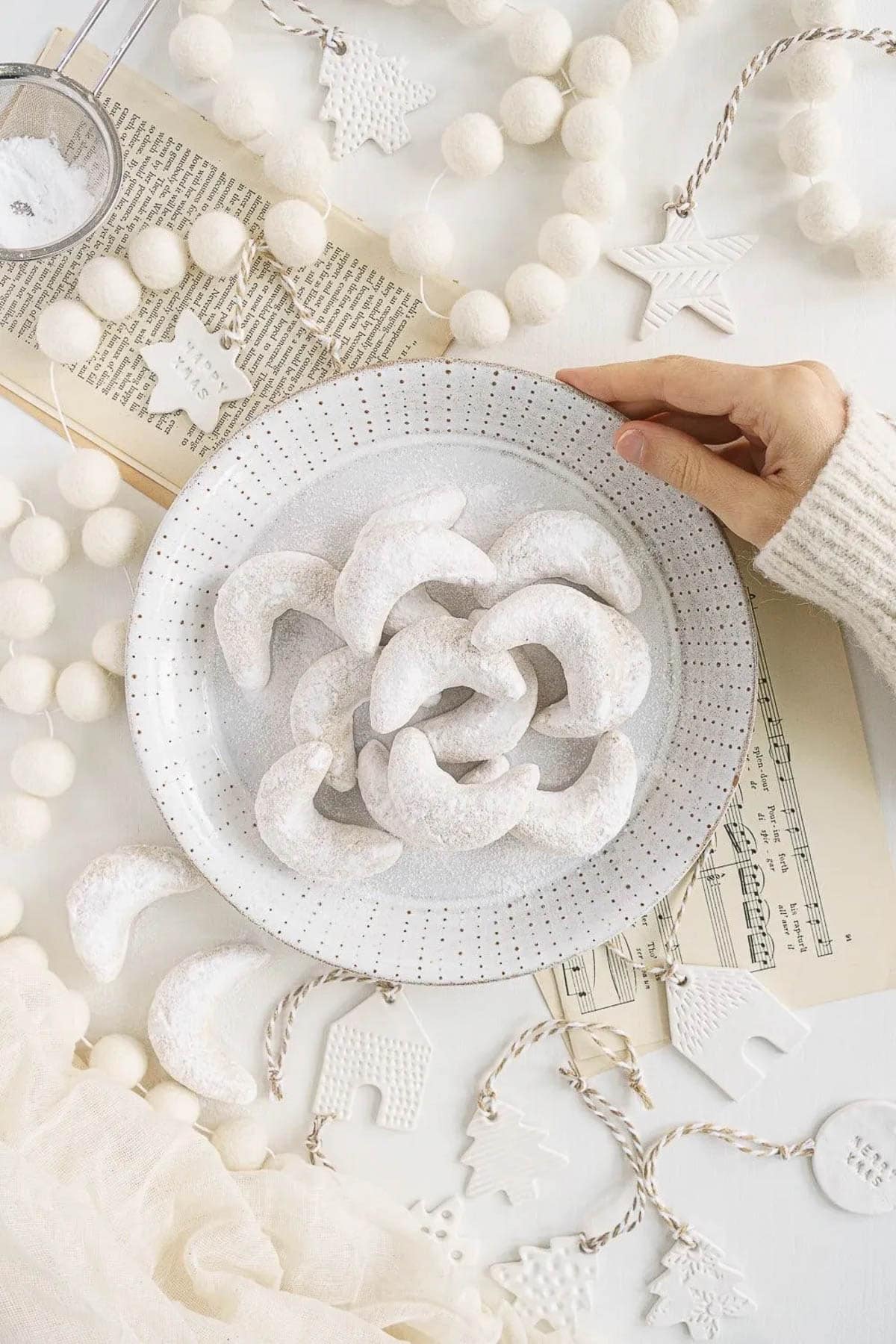A hand holding a plate of almond crescent cookies covered in powdered sugar.