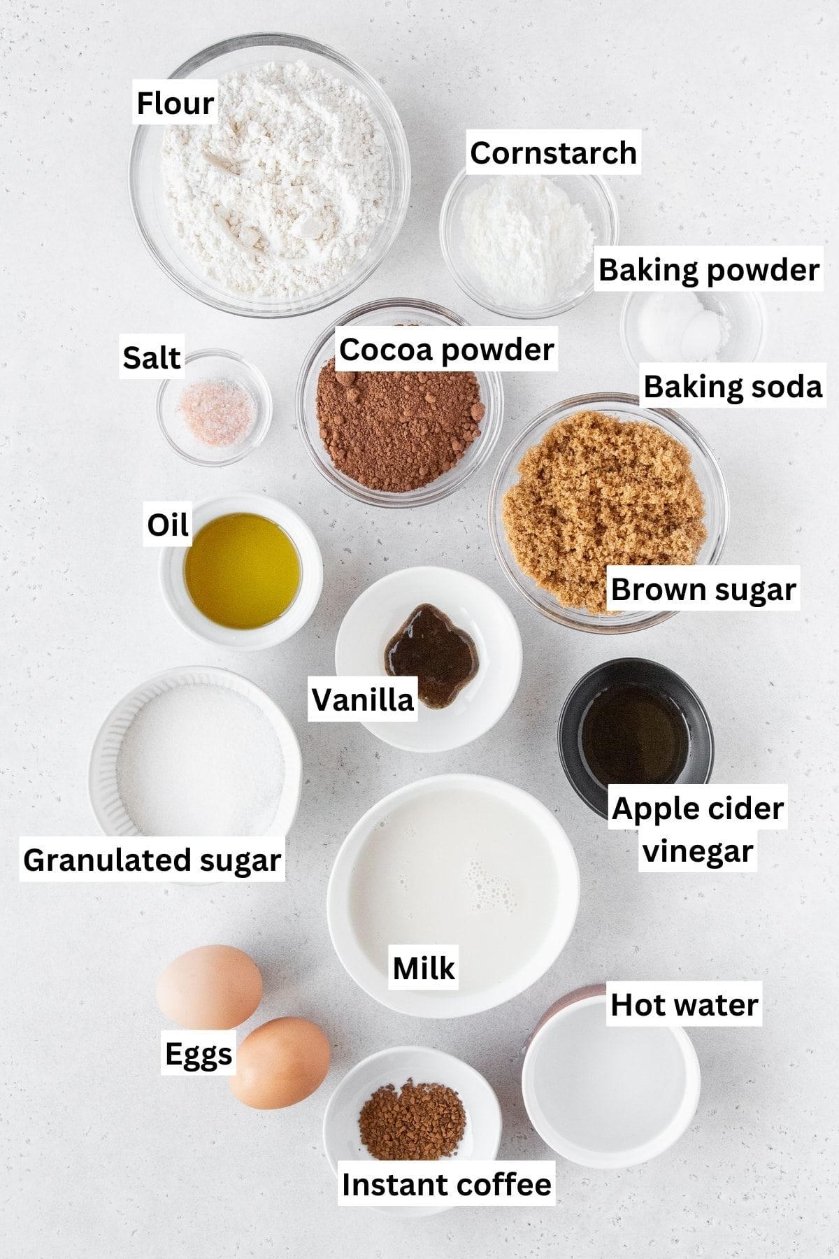 Ingredients for chocolate cupcakes measured out into bowls on a white surface.