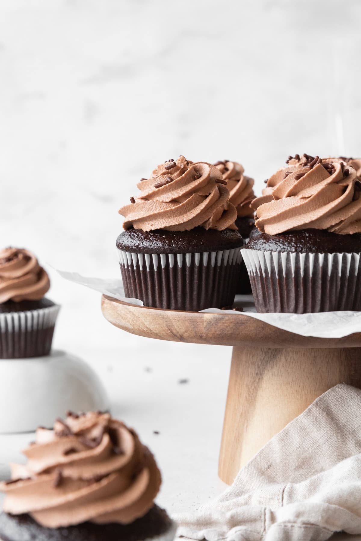 Moist chocolate cupcakes with chocolate frosting on a wooden cake stand.