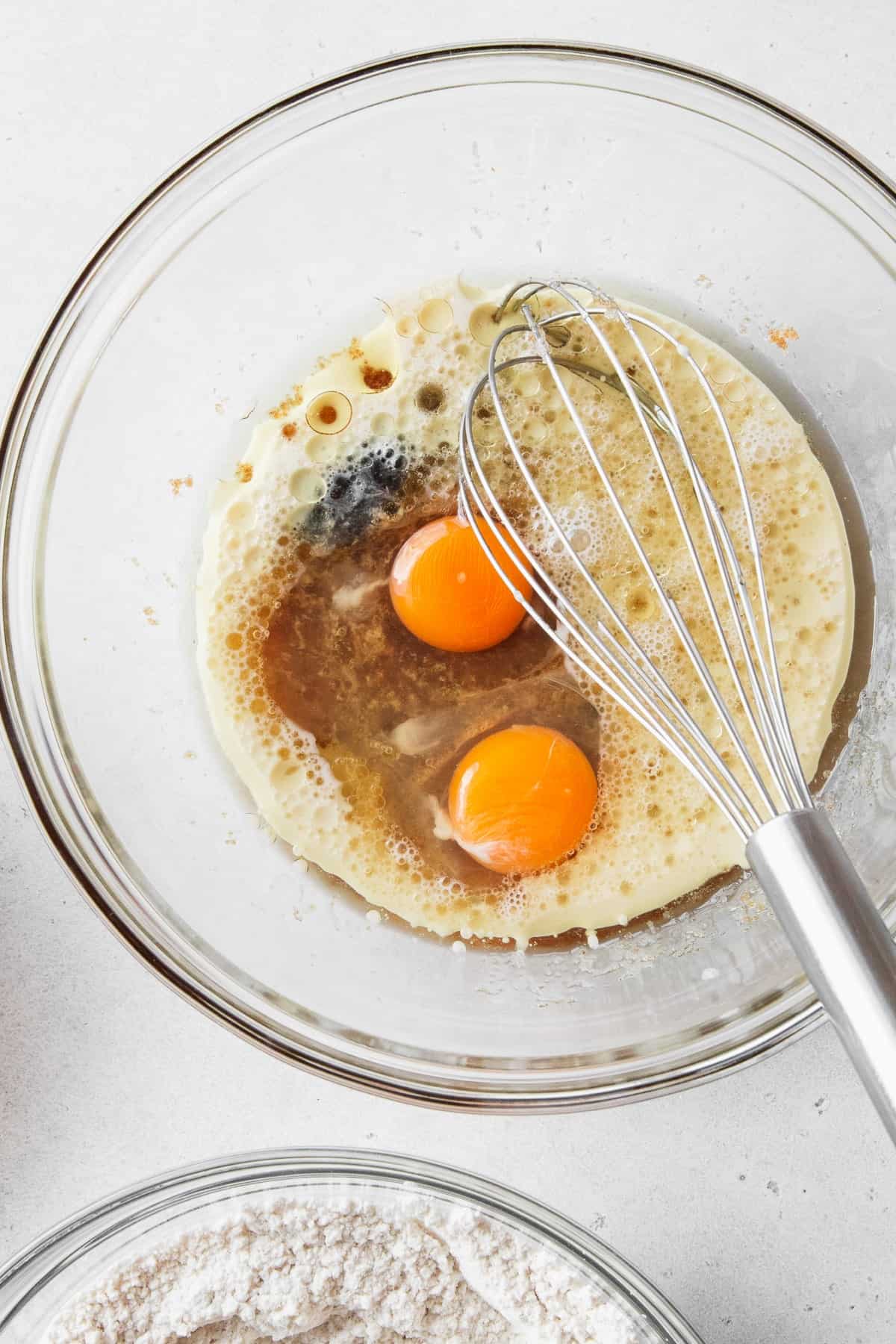 Eggs, milk, and vanilla mixed into the oil and sugar in a bowl with a whisk.