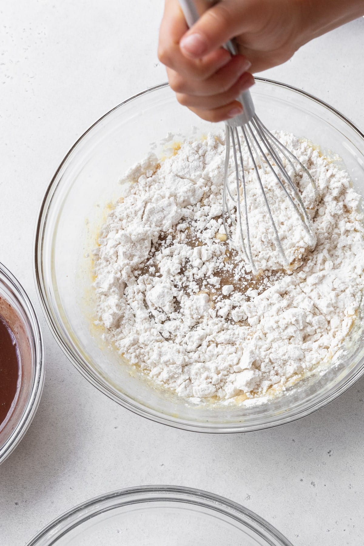 A hand whisking the dry ingredients into the wet ingredients in the glass bowl.