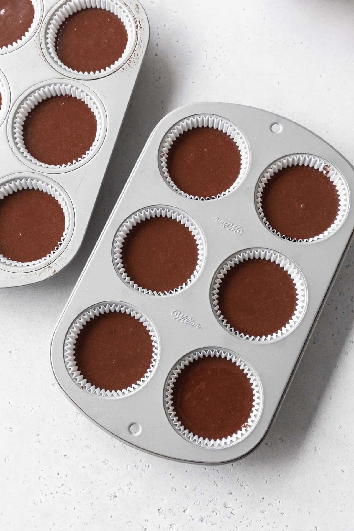 Muffin pans with chocolate cupcake batter inside.