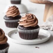 A chocolate cupcake with chocolate frosting on a white dessert plate.