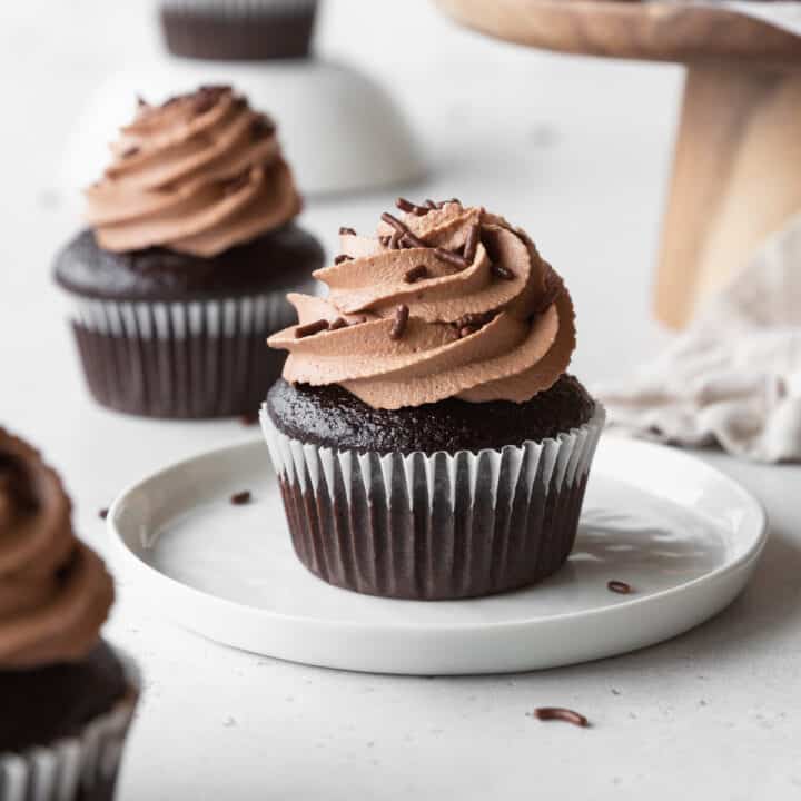 A chocolate cupcake with chocolate frosting on a white dessert plate.